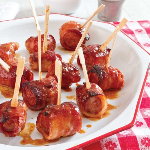 Cola Glazed Conecuh Sausage wrapped in bacon on a plate